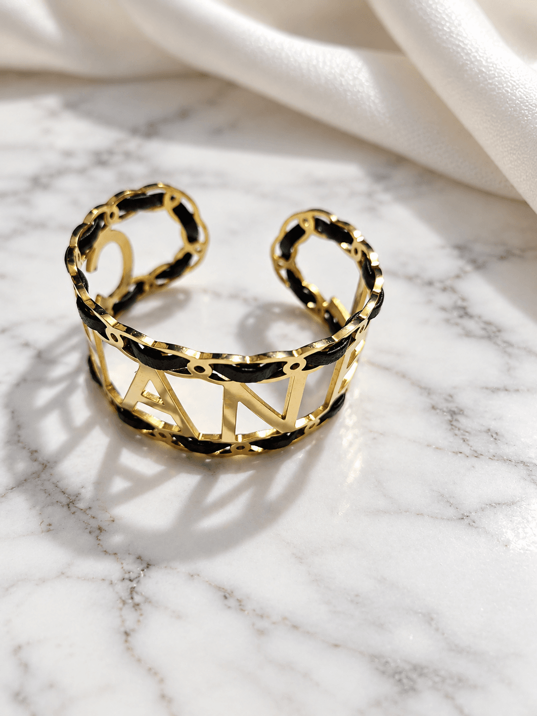 Black leather and gold letter cuff kada on marble