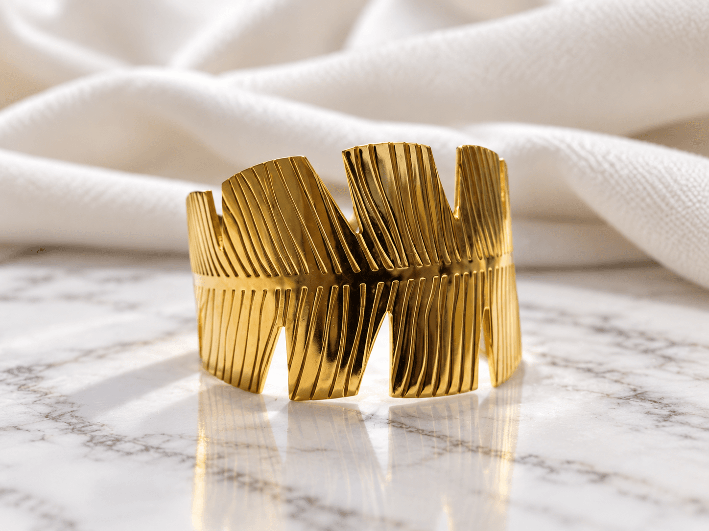 Gold sculptural ribbed cuff kada on marble with ivory shawl