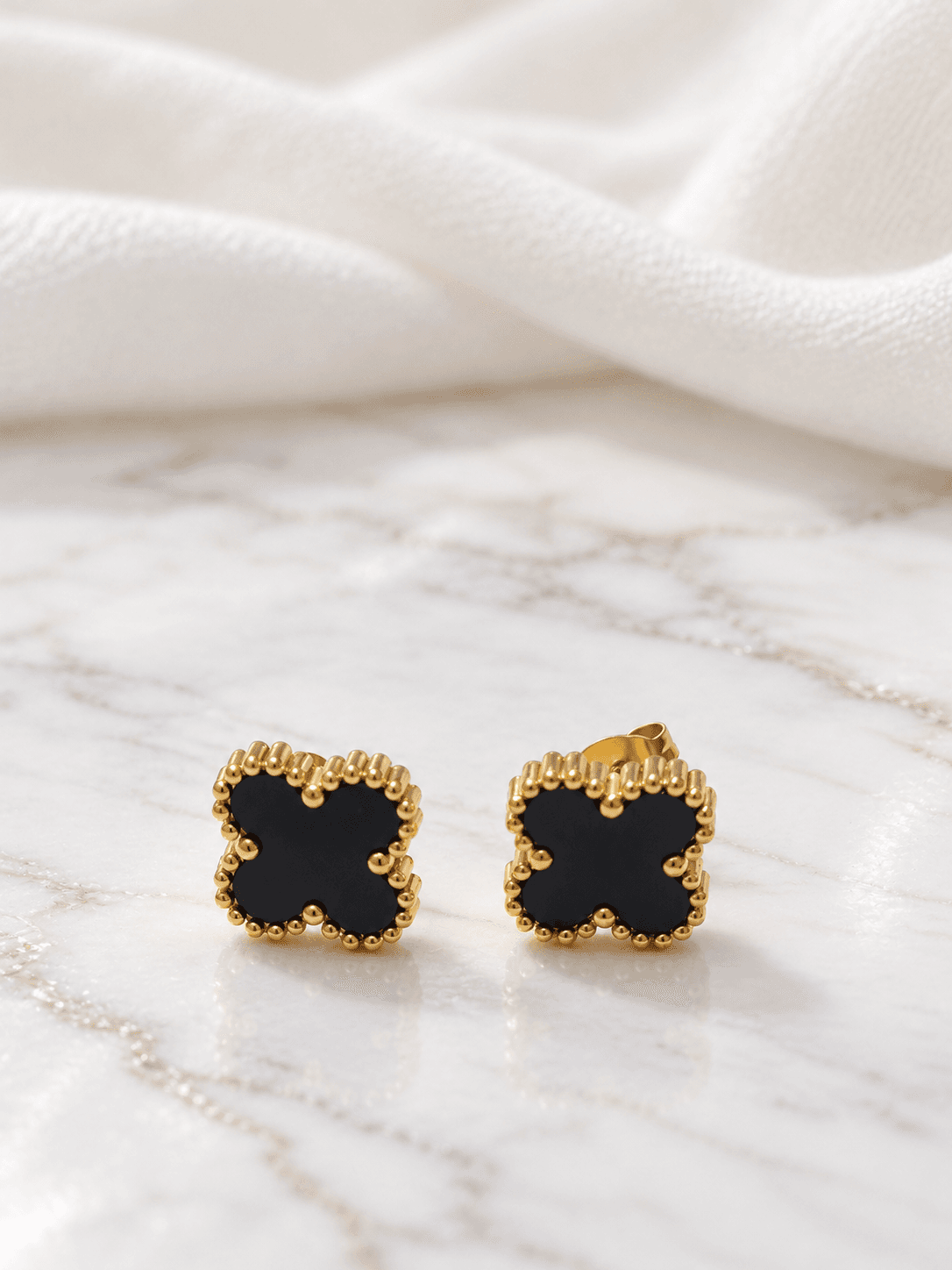 Black clover stud earrings on white marble