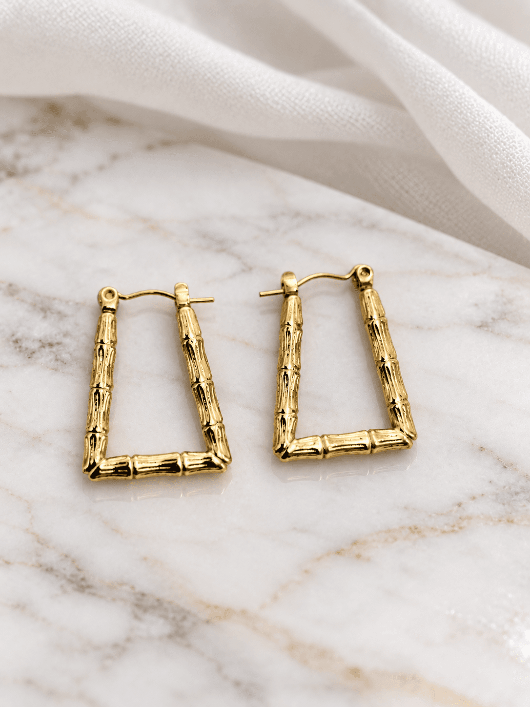 Gold bamboo rectangle hoop earrings on white marble