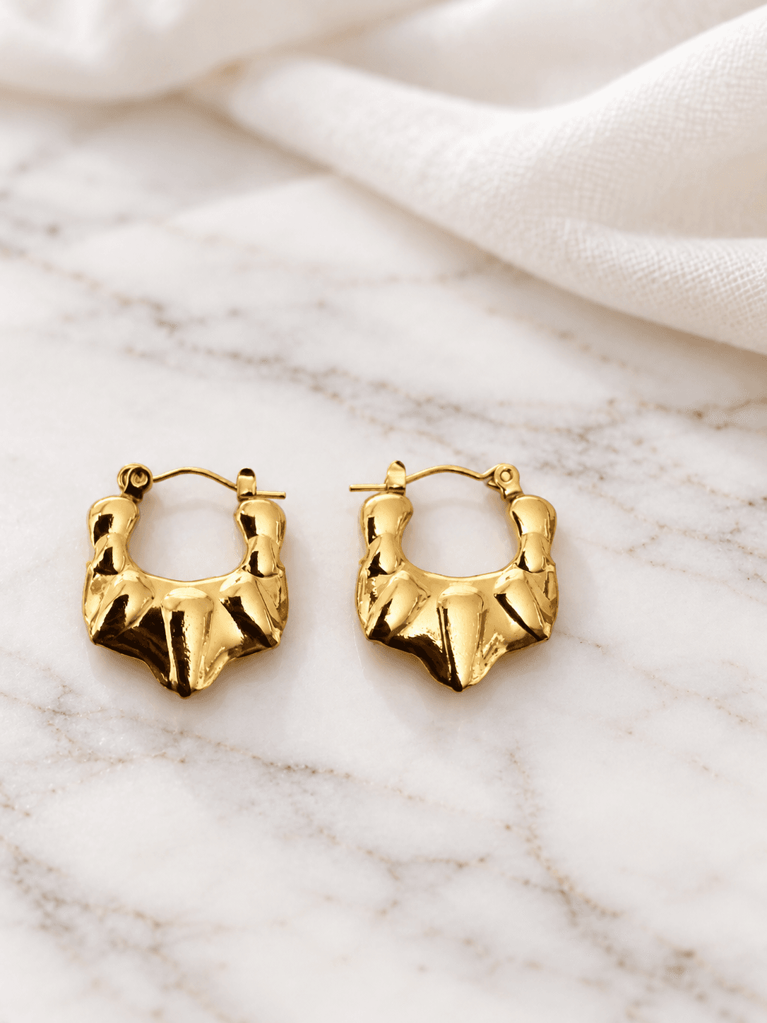 Gold chunky sculptural hoop earrings on white marble