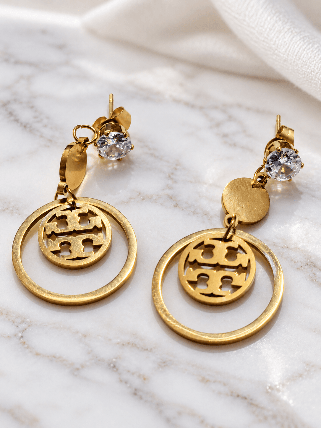 Gold cutout medallion drop earrings on marble and silk