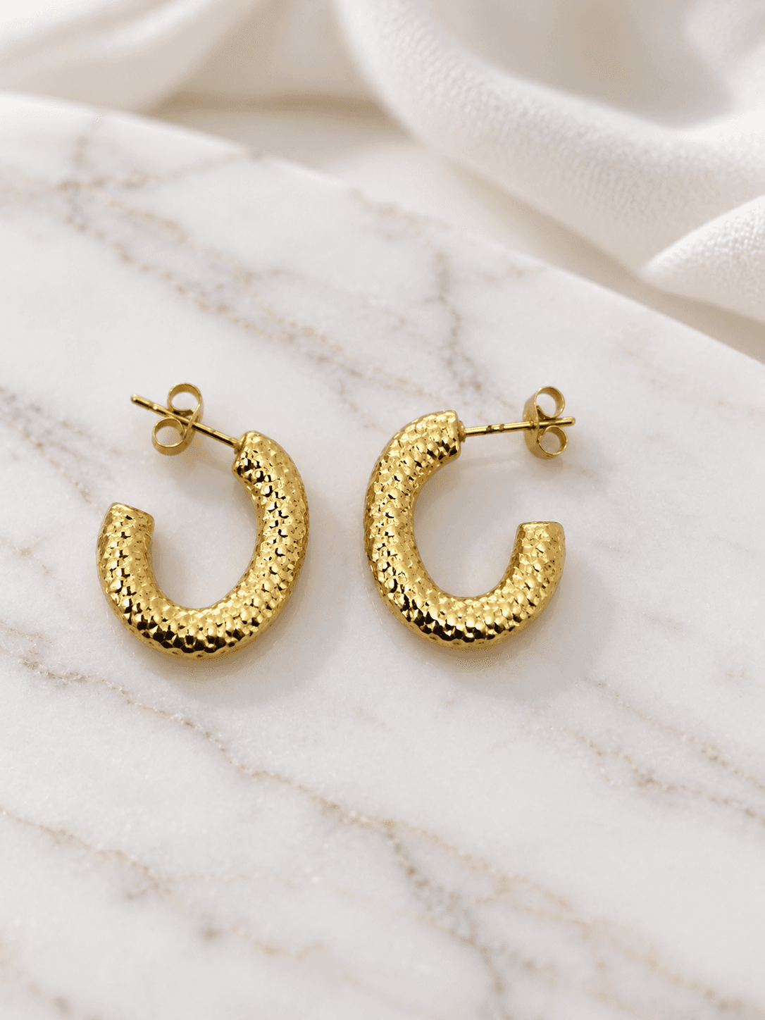 Gold diamond-textured hoop earrings on white marble