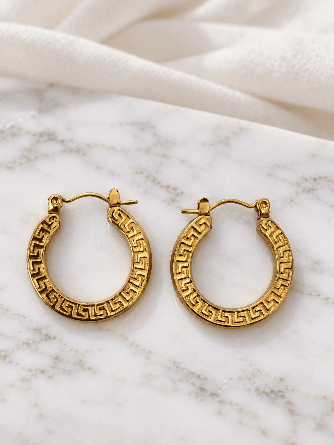 Gold greek key hoop earrings on matte white marble