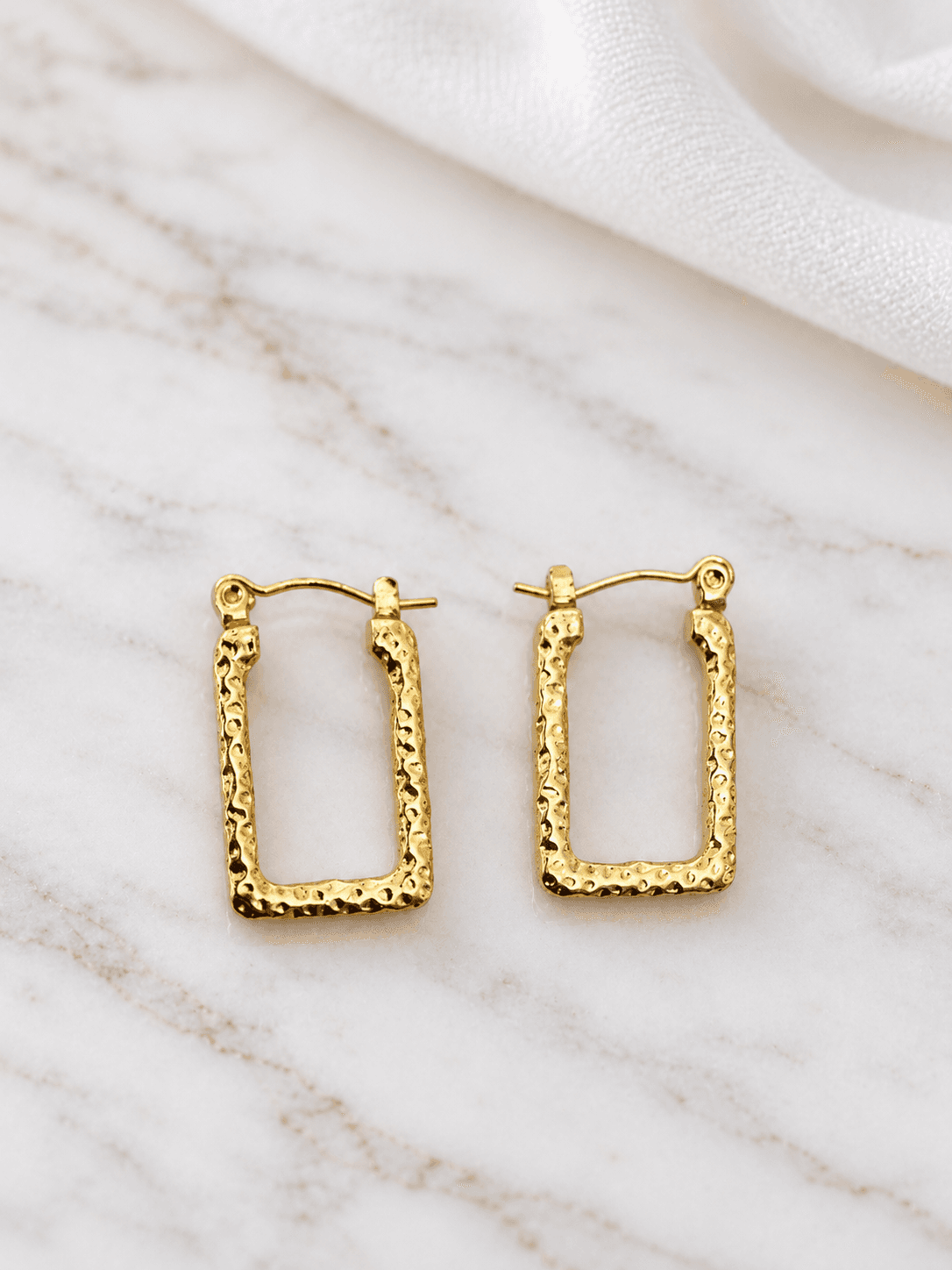 Gold hammered rectangle hoop earrings on white marble
