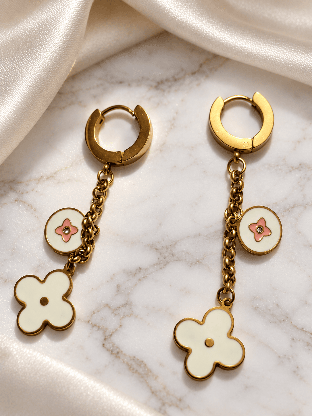 Gold huggie earrings with floral clover charms on marble