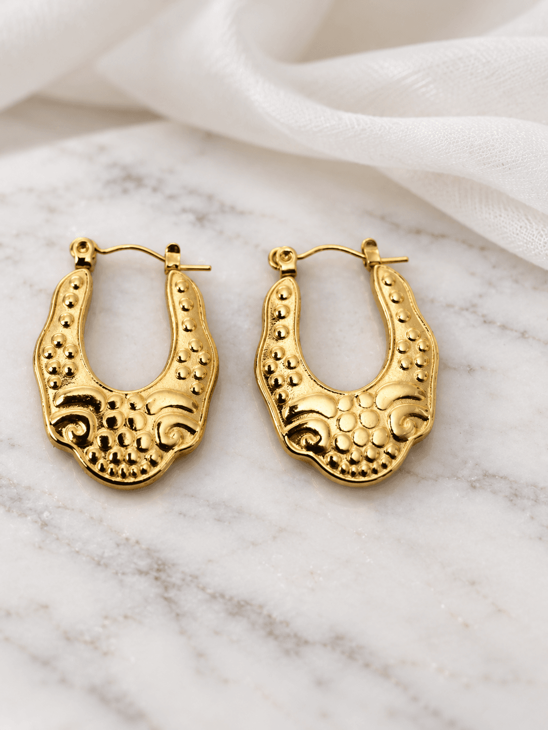 Gold ornate locket hoop earrings on white marble