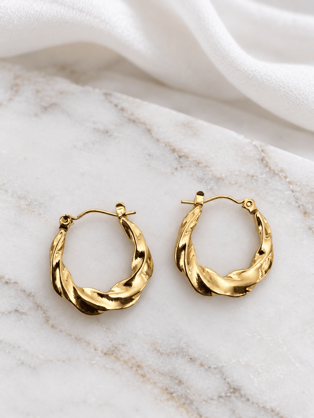 Gold smooth twisted oval hoop earrings on white marble