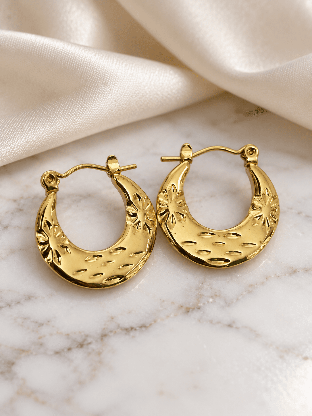 Gold star-engraved crescent hoop earrings on marble and silk