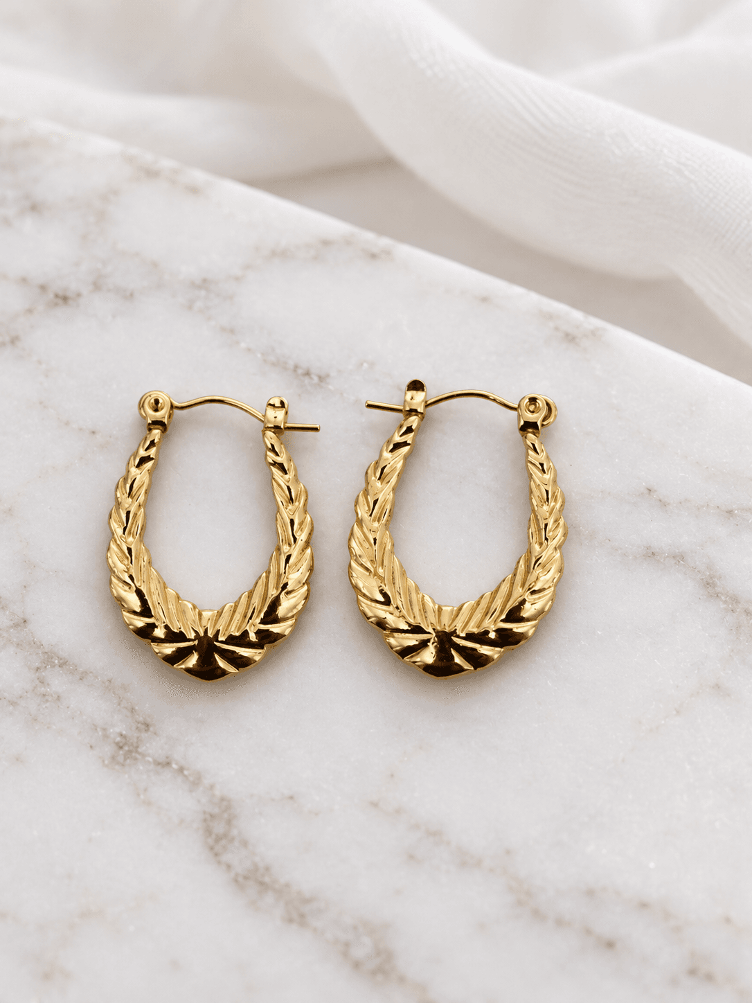Gold sunburst oval hoop earrings on white marble
