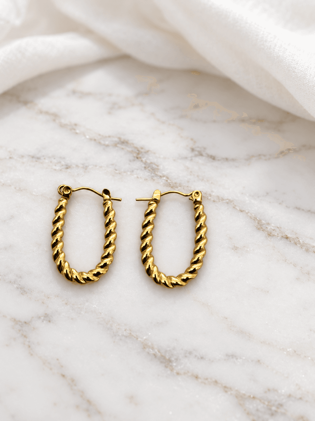 Gold twisted rope oval hoop earrings on white marble