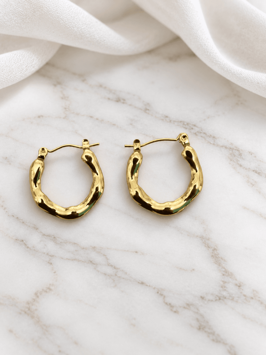 Gold wavy hoop earrings on white marble