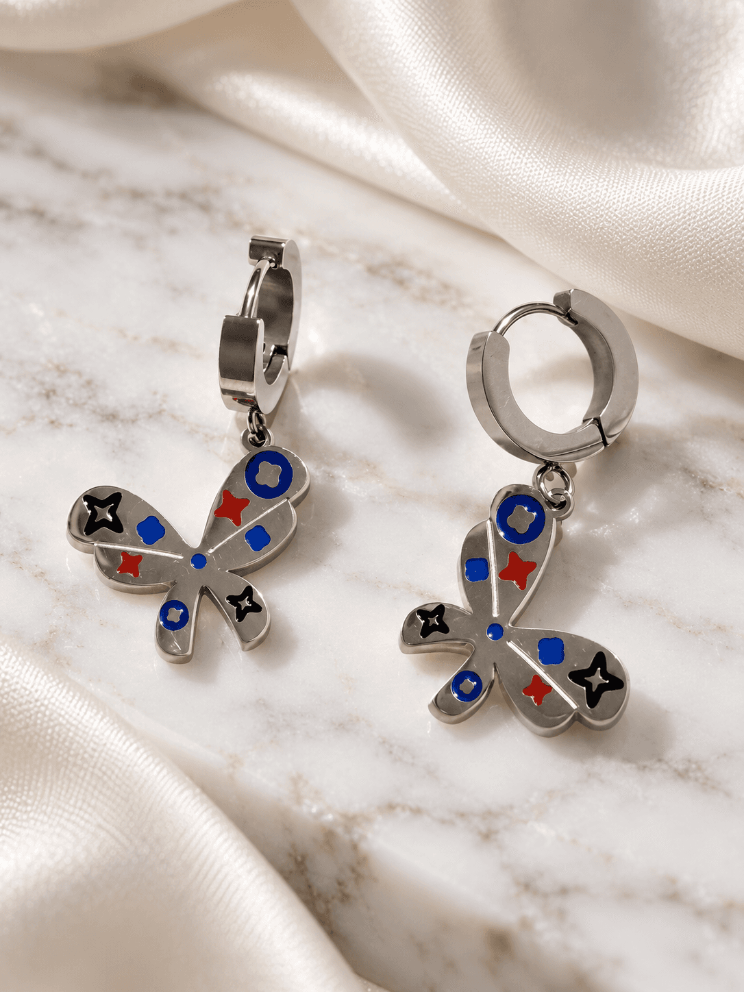 Silver butterfly enamel huggie earrings on marble